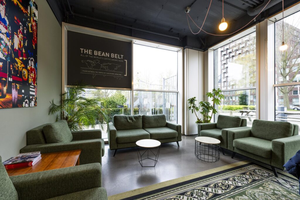 Modern lounge area with green armchairs, indoor plants, and large windows at Laan van Kronenburg.